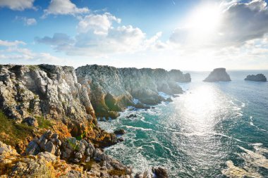 Pointe de Pen-Hir 'in kayalık sahili, uçurumlara yakın. Bulutlu mavi gökyüzü, masmavi su, fırtınalı dalgalar. Dramatik bulut manzarası. Crozon Yarımadası, Britanya, Fransa