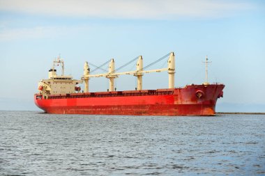 Europoort 'tan denize açılan bir vinçle büyük kırmızı bir yük gemisi (kargo gemisi). Açık mavi gökyüzü ve sirrus bulutları. Rotterdam, Hollanda. Küresel iletişim, lojistik, endüstri teması
