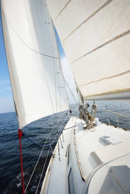 Güneşli bir yaz gününde beyaz bir yat denize açılıyor. Güverteden pruvaya, direğe ve yelkenlere kadar yukarıdan aşağı görüş. Dalgalar ve su sıçramaları. Açık mavi gökyüzü. Finlandiya Körfezi