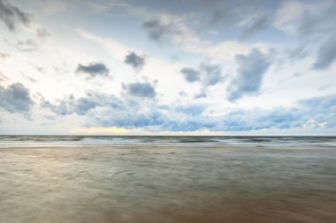 Letonya 'da fırtınadan sonra Baltık Denizi' nin üzerinde epik bir şekilde parlayan günbatımı bulutları. Kumlu sahilden bir manzara. Dramatik deniz manzarası. Kavramsal görüntü, uzun pozlama. Resim gibi bir manzara.