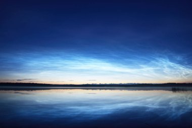 Yaz gündönümü gecesinde Saimaa Gölü 'nün üzerinde gece parlayan bulutlar ve sis vardı. Ağaç siluetleri. Altın güneş ışığı. Uzun pozlama. Destansı bulut manzarası. Suyun simetri yansımaları. Finlandiya