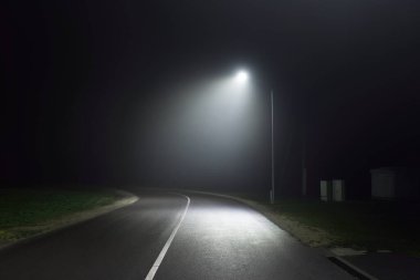 Gece sisli ve keskin bir dönüş yapan boş bir otoyol. Yol tabelası yakın plan. Karanlık şehir manzarası, şehir manzarası. Riga, Letonya. Tehlikeli sürüş, hız, özgürlük, konsept görüntü