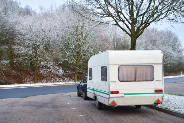 Caravan trailer and a car parked under the frosty tree. Bicycle road and city park in the background. Germany. Christmas vacations, recreation theme