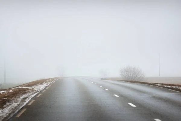 濃い白い朝の霧の中で田舎の農業分野を鋭いターンで空の高速道路 地面に新鮮な雪 危険な運転の概念 — ストック写真