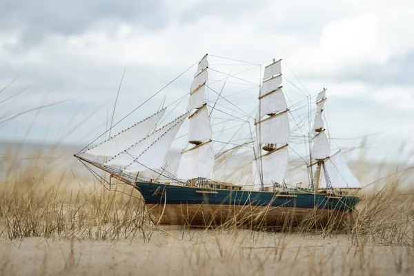 Antiquarian wooden scale model of the clipper tall ship, close-up. Dramatic sky and sea shore in the background. Traditional craft, souvenirs, hobby, collecting, vintage, modeling. Zero waste concept