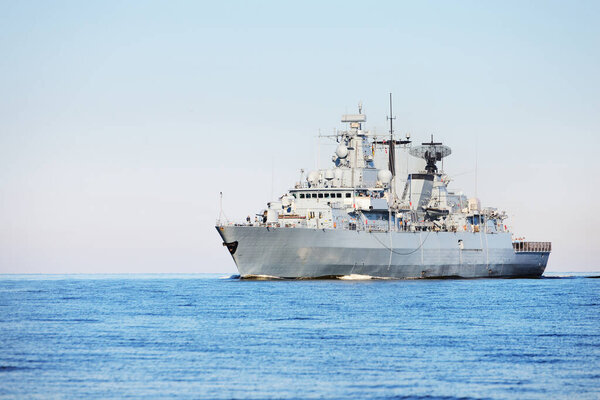 Large grey modern warship sailing in still water. Clear blue sky. Baltic sea, Germany