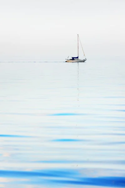 Minimalistic image of a sloop rigged yacht reflecting in a still water. Flat simple seascape. Baltic sea, Sweden