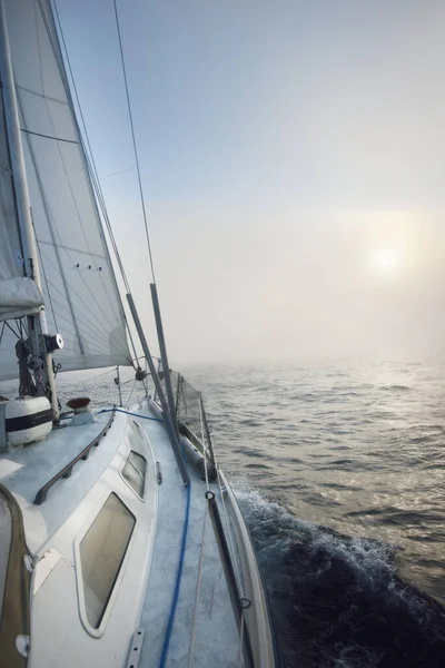 日の出の濃い霧の中で開かれたバルト海で白いヨットのセーリング スウェーデンだ デッキから弓と帆へのクローズアップビュー 朝の太陽と輝く雲 壮大な海の景色 スポーツとレクリエーションのテーマ — ストック写真