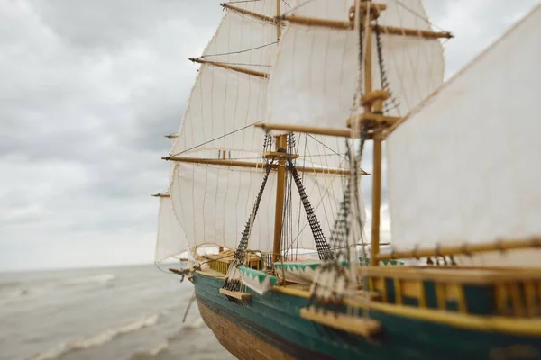 Antiquarian wooden scale model of the clipper tall ship, close-up. Dramatic sky and sea shore in the background. Traditional craft, souvenirs, hobby, collecting, vintage, modeling. Zero waste concept