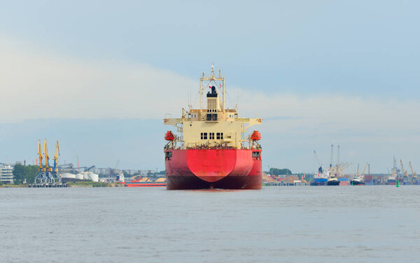 Large red bulk carrier (cargo ship) with a cranes arriving to the Europoort, close-up. Rotterdam, Netherlands. Freight transportation, global communications, logistics, industry theme