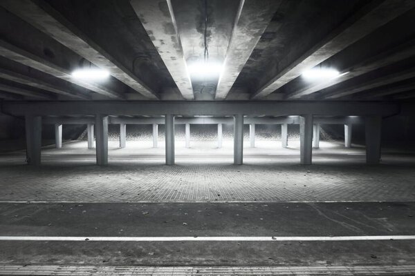 An empty illuminated motorway, bicycle road and pedestrian walkway under the bridge in a fog at night. Dark urban scene. Riga, Latvia. Dangerous driving, concept image