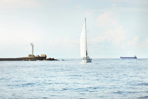 Small yacht sailing near the lighthouse on a clear day. Riga bay, Baltic sea, Latvia. Cruise, sport, recreation, leisure activity concepts