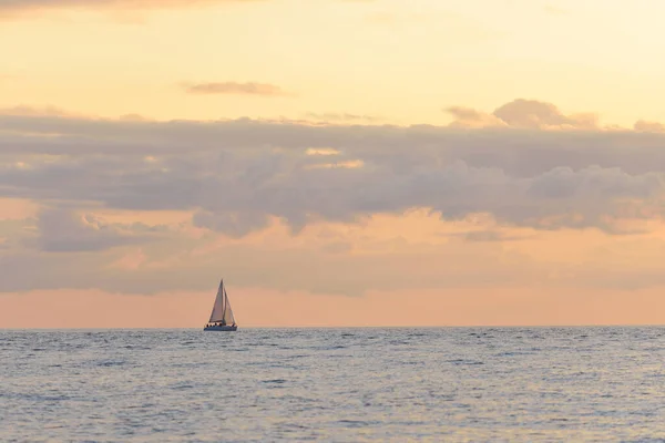 Epic sunset sky above the Baltic sea shore, sailing boat (sloop rigged yacht) close-up. Glowing golden clouds, warm sunlight. Dramatic cloudscape. Latvia