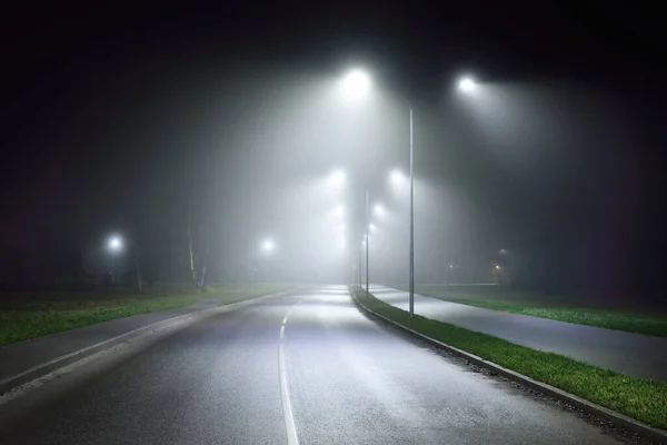 Illuminated empty asphalt road in a fog at night. Dark urban scene, cityscape. Industrial zone in Riga, Latvia. Dangerous driving, speed, freedom, concept image