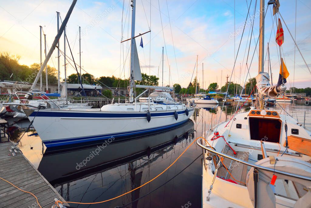 Elegant and modern modern sailing boats (for rent) moored to a pier in a yacht marina at sunset. Transportation, cruise, leisure activity, sport and recreation theme. Sweden