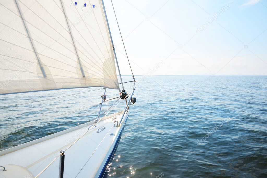 White yacht sailing on a sunny summer day. Top down view from the deck to the bow, mast and sails. Waves and water splashes. Clear blue sky. Gulf of Finland