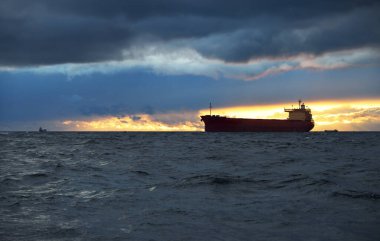 Büyük kırmızı kargo gemisi karanlık günbatımı göğünün altında açık denizde yol alıyor. Southampton 'da. İngiltere. Dramatik bulutlar, kasırga, fırtınalı hava. Küresel iletişim, nakliye, endüstri, lojistik