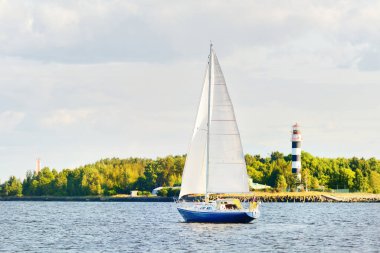 Gün batımında Riga körfezinde mavi yelkenli yelkenli yelkenli. Yakın plan. Baltık Denizi, Letonya. Arka planda deniz feneri var. Yarış, spor, eğlence, eğlence aktivitesi, takım çalışması kavramları.