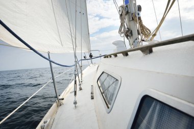 Güneşli bir yaz gününde beyaz bir yat denize açılıyor. Güverteden pruvaya, direğe ve yelkenlere yakın görüntü. Dalgalar ve su sıçramaları. Açık mavi gökyüzü. Finlandiya Körfezi