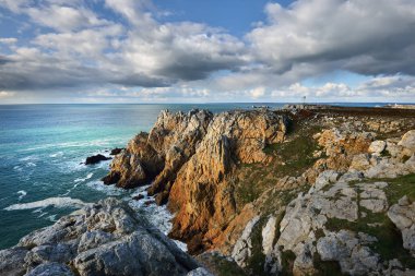 Pointe de Pen-Hir 'in kayalık sahili, uçurumlara yakın. Bulutlu mavi gökyüzü, masmavi su, fırtınalı dalgalar. Dramatik bulut manzarası. Crozon Yarımadası, Britanya, Fransa