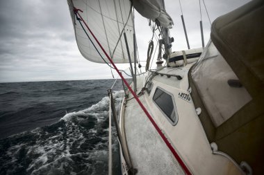 Yağmurlu bir günde, fırtınalı bir havada yat gezintisi. Güverteden pruvaya, direğe ve yelkenlere yakın görüntü. Dramatik fırtınalı gökyüzü, kara bulutlar. Dalgalar ve su sıçramaları. Kötü hava. Baltık Denizi, İsveç