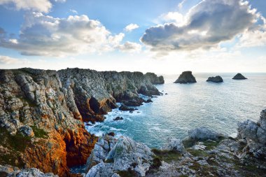 Pointe de Pen-Hir 'in kayalık sahili, uçurumlara yakın. Bulutlu mavi gökyüzü, masmavi su, fırtınalı dalgalar. Dramatik bulut manzarası. Crozon Yarımadası, Britanya, Fransa