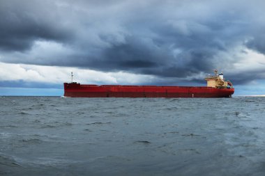 Büyük kırmızı kargo gemisi karanlık günbatımı göğünün altında açık denizde yol alıyor. Southampton 'da. İngiltere. Dramatik bulutlar, kasırga, fırtınalı hava. Küresel iletişim, nakliye, endüstri, lojistik
