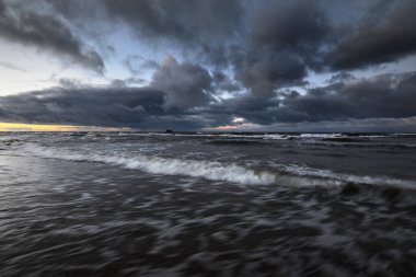 Kışın Baltık Denizi 'nin üzerindeki fırtına bulutları, uzun pozlama. Dramatik günbatımı gökyüzü, dalgalar ve su sıçramaları. Koyu deniz manzarası. Almanya