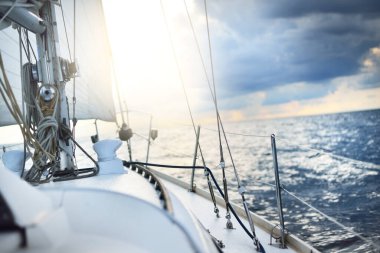 Beyaz yat gün batımında açık denizde yüzüyor. Güverteden pruva ve yelkenlere kadar yakın çekim. Fırtınadan sonra renkli bulutlarla dramatik bir gökyüzü. Dalgalar ve su sıçrıyor. Spor ve eğlence teması