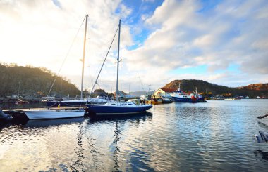 Sürat tekneleri, yelkenliler ve balıkçı tekneleri fiyortlardaki küçük bir köyde rıhtıma demirlediler. Hidra Adası, Rogaland bölgesi, Norveç. Geleneksel mimari. Dramatik akşam gökyüzü. Seyahat hedefleri teması