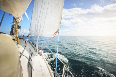 Güneşli bir günde beyaz bir yat gezintisi. Güverteden pruva ve yelkenlere kadar yukarıdan aşağıya doğru. Dalgalar ve su sıçramaları. Açık mavi gökyüzü. Kuzey denizi, Norveç. Ulaşım, spor, eğlence teması