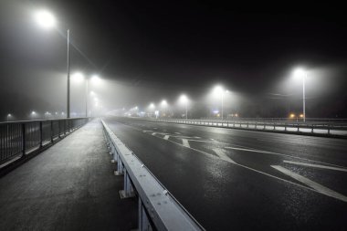 Gece sisli bir havada karayolu yakınında boş bir bisiklet yolu (yaya geçidi). Fenerler yakın plan. Ulaşım, tehlikeli sürüş, eğlence ve sağlıklı yaşam tarzı teması. Riga, Letonya