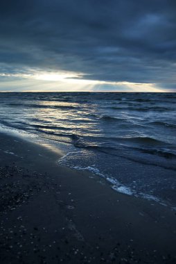 Dramatik günbatımı bulutları altında fırtınalı Baltık Denizi. Kumlu sahilden bir manzara. Riga Körfezi, Letonya. Destansı deniz manzarası. Karanlık sonbahar sahnesi. Meteoroloji, ekoloji, çevre koruma, iklim değişikliği