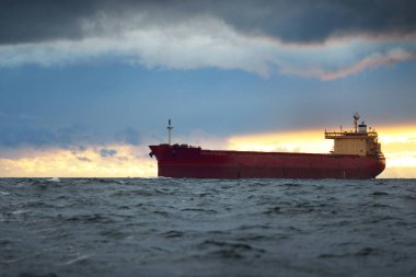 Büyük kırmızı kargo gemisi karanlık günbatımı göğünün altında açık denizde yol alıyor. Southampton 'da. İngiltere. Dramatik bulutlar, kasırga, fırtınalı hava. Küresel iletişim, nakliye, endüstri, lojistik