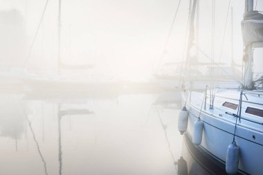Yelkenli tekneler, güneşin doğuşunda yoğun beyaz bir sisle bir rıhtıma demirlediler. Kiel, Almanya 'daki yat kulübü. Spor, eğlence, ulaşım teması