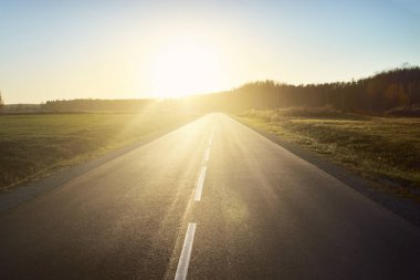 Sıcak bir yaz gününde gün batımında açık bir otoyol. Arka planda orman var. Kırsal alanlarda araba sürmek. Boş zaman aktivitesi, eğlence teması. Letonya