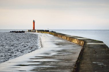 Güneş bataryasıyla turuncu deniz fenerine doğru renkli günbatımına karşı boş bir gezinti. Şaşırtıcı bulut manzarası. Uzun pozlama. Çevre koruma teması. Baltık Denizi, Riga Körfezi, Letonya