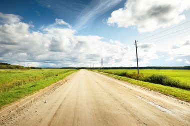 Yağmurdan sonra tarlalardan geçen boş bir köy yolu. Dramatik gökyüzü, destansı bulutlar. Hava kararsız. Transformatör direkleri yakın çekim. Letonya