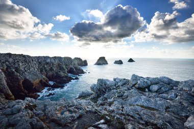 Pointe de Pen-Hir 'in kayalık sahili, uçurumlara yakın. Bulutlu mavi gökyüzü, masmavi su, fırtınalı dalgalar. Dramatik bulut manzarası. Crozon Yarımadası, Britanya, Fransa
