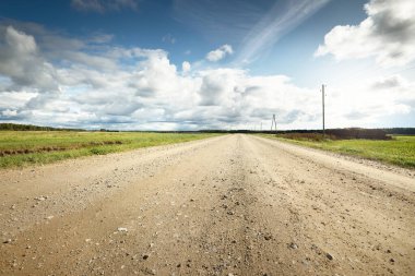 Yağmurdan sonra tarlalardan geçen boş bir köy yolu. Dramatik gökyüzü, destansı bulutlar. Hava kararsız. Transformatör direkleri yakın çekim. Letonya
