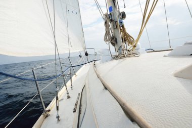 Güneşli bir yaz gününde beyaz bir yat denize açılıyor. Güverteden pruvaya, direğe ve yelkenlere yakın görüntü. Dalgalar ve su sıçramaları. Açık mavi gökyüzü. Finlandiya Körfezi