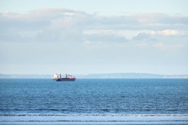 Kargo gemisi Douarnenez Körfezi 'nin kıyısından geçiyor. Açık mavi gökyüzü. Sudaki yansımalar. Dalgalar ve su sıçramaları. Brittany, Fransa. Seyahat yerleri, küresel iletişim teması