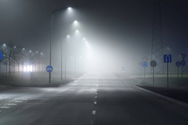 Gece sisli bir ortamda bomboş bir otoyol. Sokak lambaları ve yol işaretleri yakın. Karanlık şehir manzarası, şehir manzarası. Riga, Letonya. Tehlikeli sürüş, hız, özgürlük, konsept görüntü