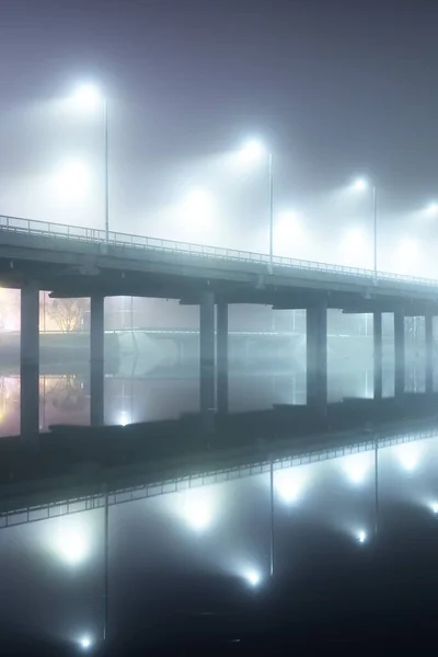 夜霧の中で照明された空の道路橋の低角度ビュー 提灯を閉じます 水の対称性の反射 自然の鏡 ラトビアのリガのドーヴァ川 — ストック写真