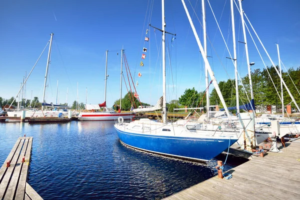 Elegant and modern sailing boats (for rent) moored to a pier in a yacht marina on a clear day. Transportation, sport and recreation theme. Sweden. Blue sloop rigged sailboat close-up