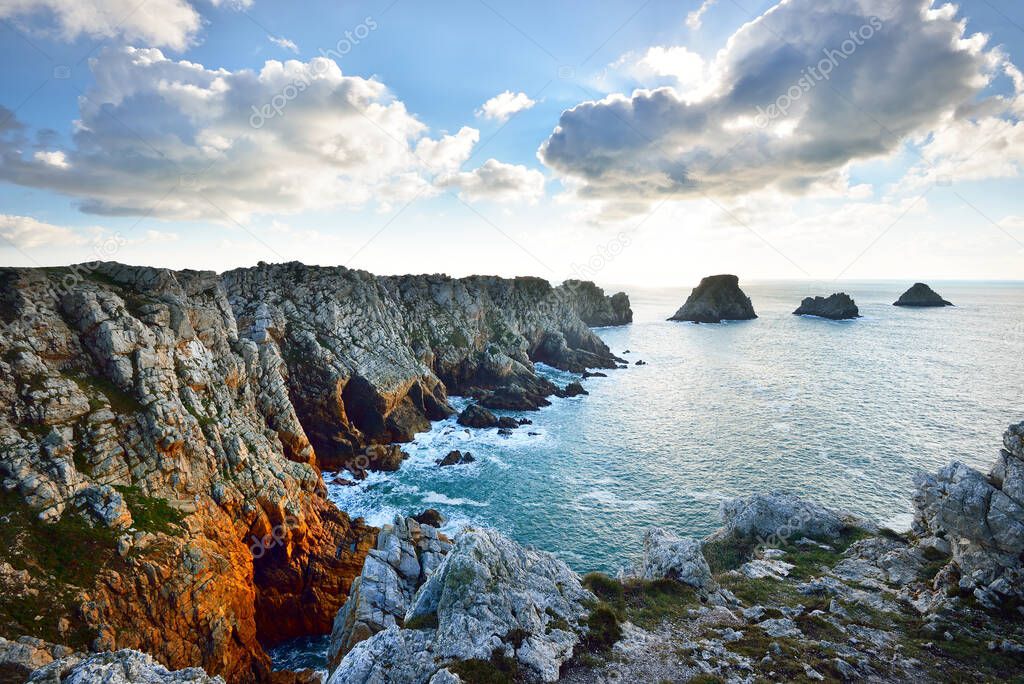 Aerial view of the rocky shore of Pointe de Pen-Hir, cliffs close-up. Cloudy blue sky, azure water, stormy waves. Dramatic cloudscape. Crozon peninsula, Brittany, France