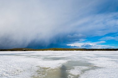 Karla kaplı donmuş Kuito gölünün üzerindeki dramatik mavi gökyüzü, arka planda kozalaklı orman. Kış kır manzarası. Fırtına bulutları. Karelya Kuzey, Laponya