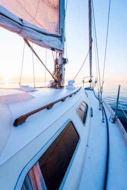 Sakin su. Günbatımında beyaz yelkenli tekneyle denize açılacak. Güverteden pruvaya, direğe ve yelkenlere bir manzara. Baltık Denizi, Letonya