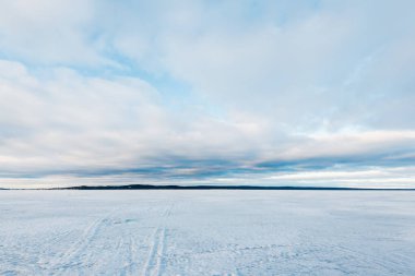 Kış manzarası. Gün batımında donmuş karla kaplı göl manzarası. Arka planda orman var. Renkli akşam bulutları. Onega Gölü, Karelia, Rusya