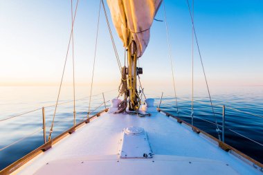 Sakin su. Günbatımında beyaz yelkenli tekneyle denize açılacak. Güverteden pruvaya, direğe ve yelkenlere bir manzara. Baltık Denizi, Letonya